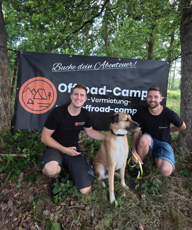 Marvin und Michael, Gründer von Offroad Camper, mit Hund vor dem Firmenbanner
