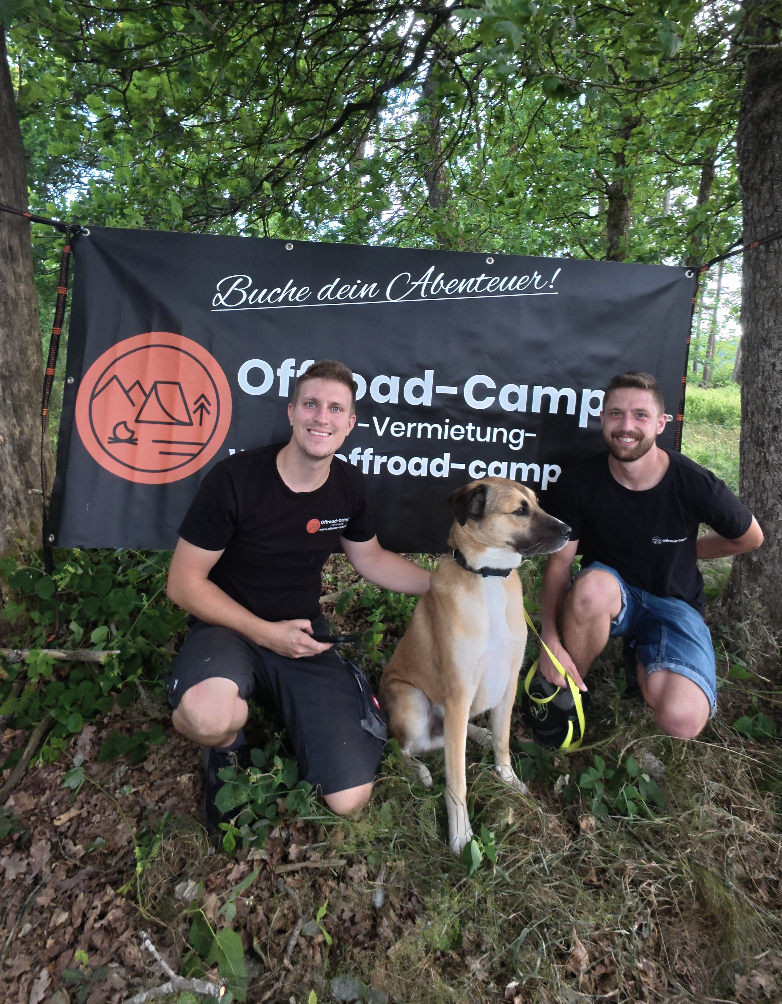 Marvin und Michael mit Hund vor Offroad-Camper Banner