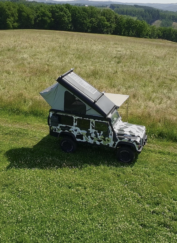 Defender mit geöffnetem Dachzelt auf einer Wiese